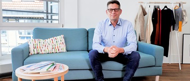 Ulrich Plein, Leiter der Geschäftsstelle des Textilsiegels Grüner Knopf, sitzt auf einem Sofa.