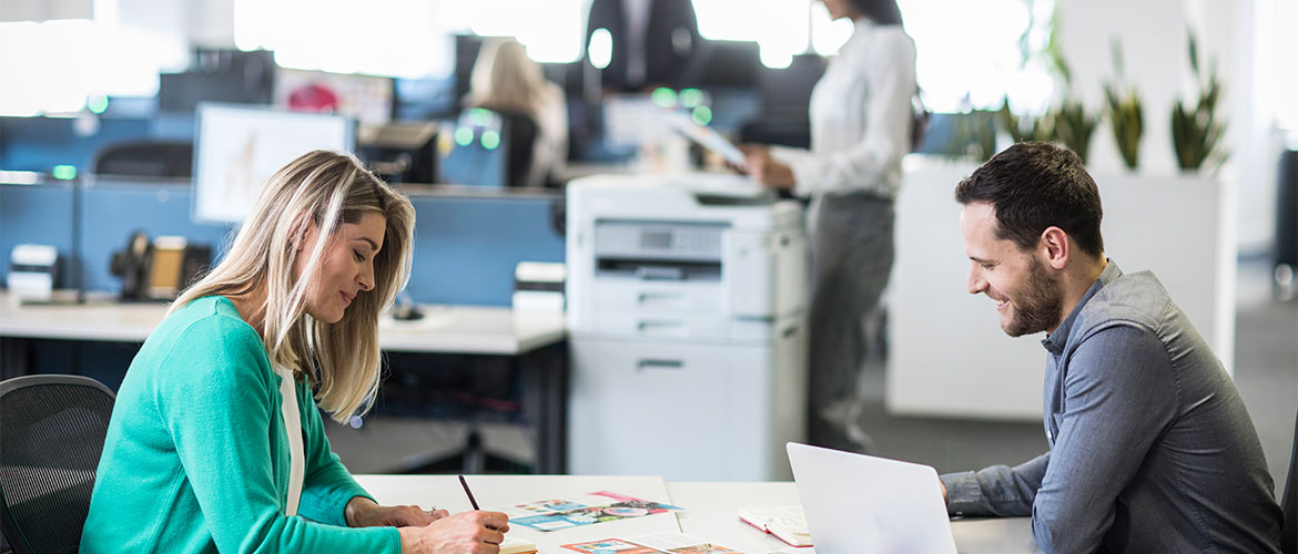 Zwei Menschen im Büro am Schreibtisch, Drucker im Hintergrund