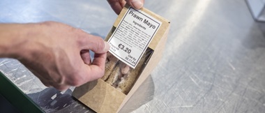 Zwei Hände, die Sandwichverpackungen mit trägerlosen Etiketten versehen.