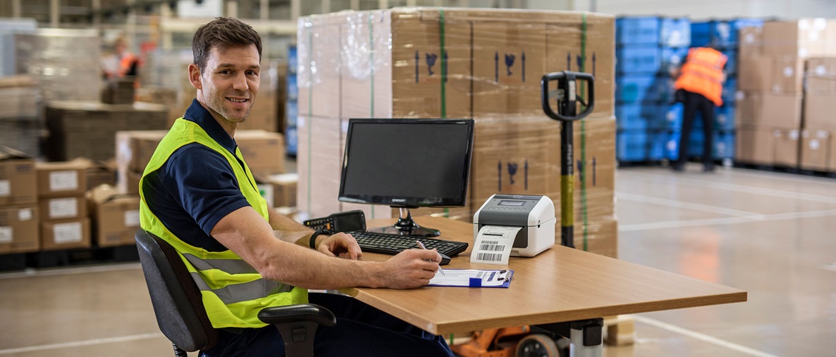 Mann sitzt am Schreibtisch im Logistikzentrum und druckt Versandetiketten aus