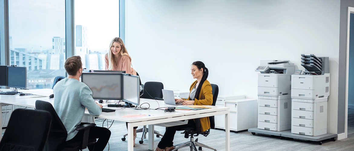 Drei Frauen und ein Mann arbeiten in einem Büro. Brother Drucker im Hintergrund.