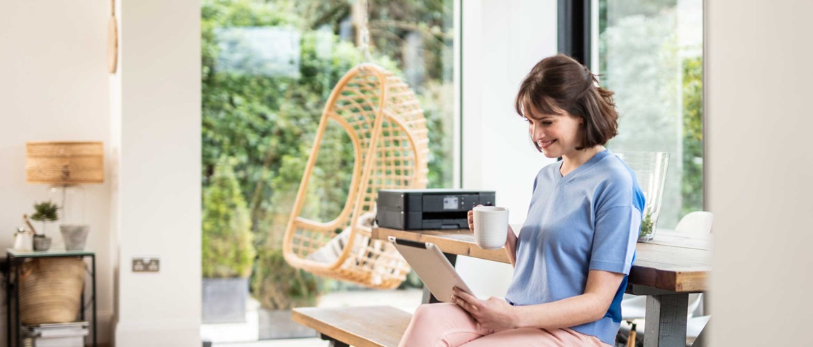 Einer Frau hält ein Apple Tablet in der Hand. Ein AirPrint Drucker von Brother steht im Hintergrund auf dem Tisch.