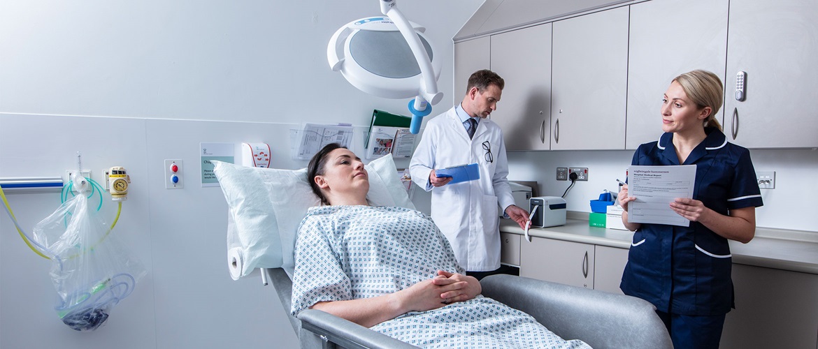 Patientenin Liegt im Behandlungszimmer und Unterhält Sich mit einem Krankenschwester, der Arzt im Weißen Kittel drucken ein Etikett AUS.
