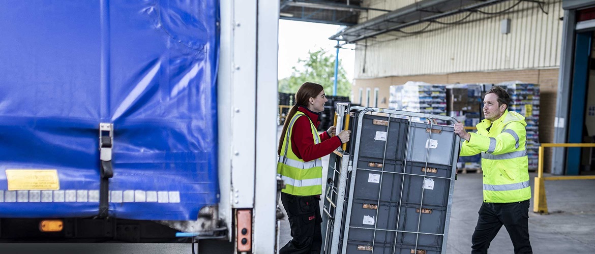 Direte Filialzustelung, Zwei Lagerarbeit in Warnwesten Schieben Graue Kisten Auf Die Rückseite Einen Lastwagens