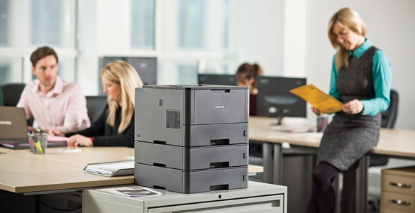 Brother-Drucker im Vordergrund. Drei Personen in einem Büro im Hintergrund.