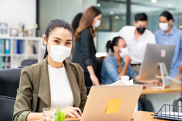 Frau am Computer mit Maske im Büro