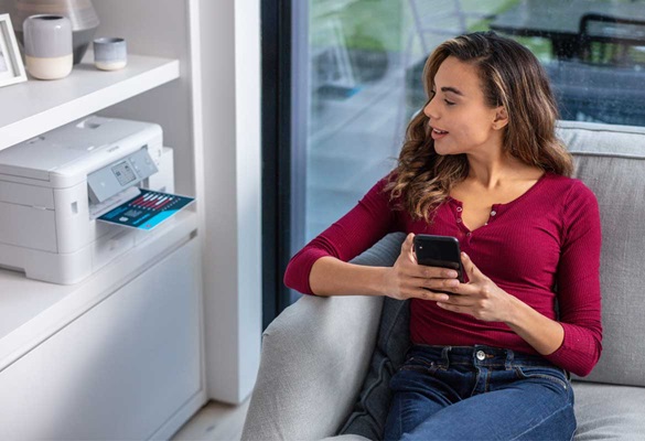 Eine Frau sitzt auf der Couch und druckt über einen AirPrint Drucker etwas aus