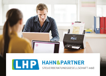 Mann und Frau, ein Bürotisch sitzend, Brotherscanner auf dem Tisch, Aktenordner im Hintergrund