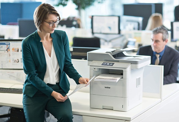 Frau mit Brille und Grünem Anzug sitzt am Tisch Neben Brother MFC-L6900DW Drucker, Mann mit Anzug, Monitore, Schreibtische