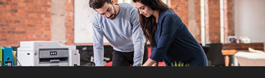 Zwei Personen unterhalten sich. Brother Drucker mit Managed Print Service im Hintergrund.