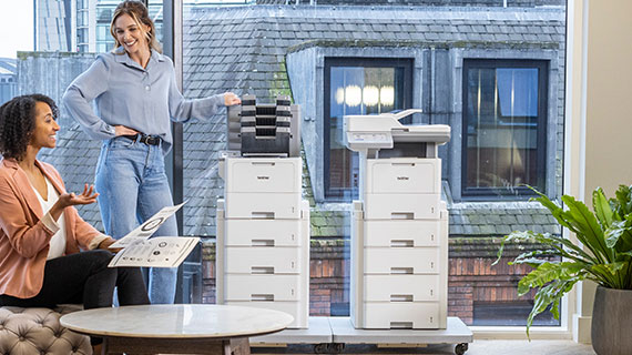 Zwei Fruen in einem Büro mit Ausdrucken in der Hand, im Hintergrund stehen zwei Brother Drucker