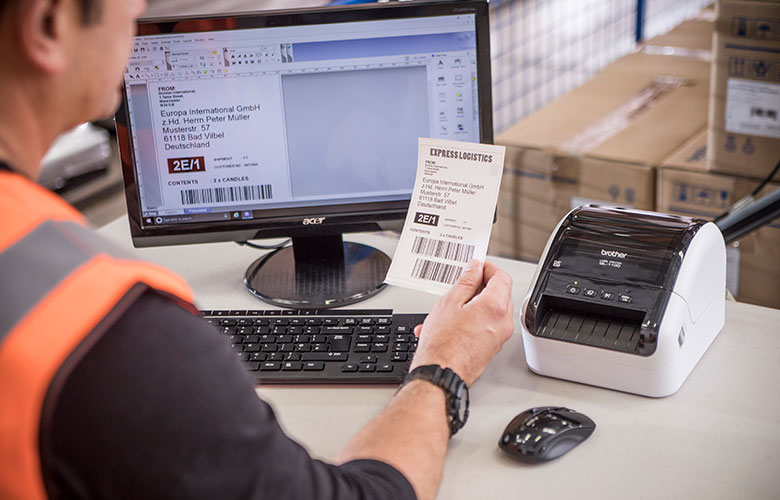 Brother QL-Drucker neben dem Monitor mit Versandetikett im Lager gedruckt
