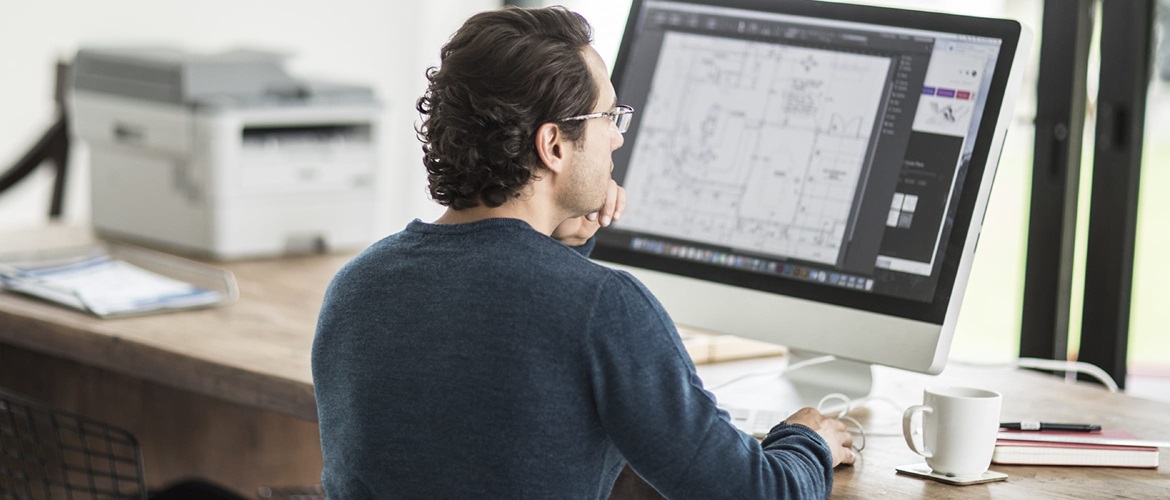 Ein Mann druckt ein Dokument von einem All-in-One-Computer, während er an einem Schreibtisch in einer Home-Office-Umgebung sitzt.