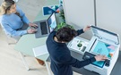 Mann an einem Drucker und Frau an einem Laptop