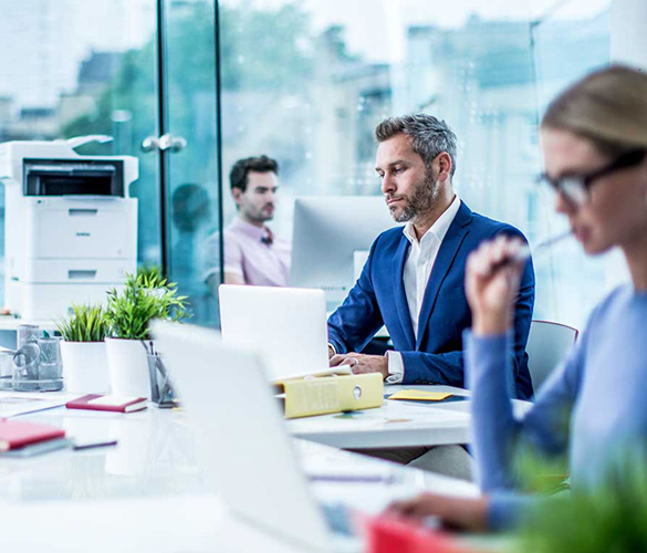 Drei Personen sitzen an Schreibtischen in einem Büro mit einem Drucker