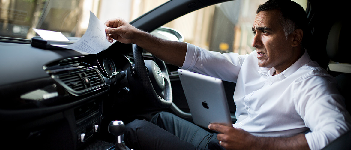 Mann druckt im Auto über Tablet ein Dokument über mobilen Drucker aus.
