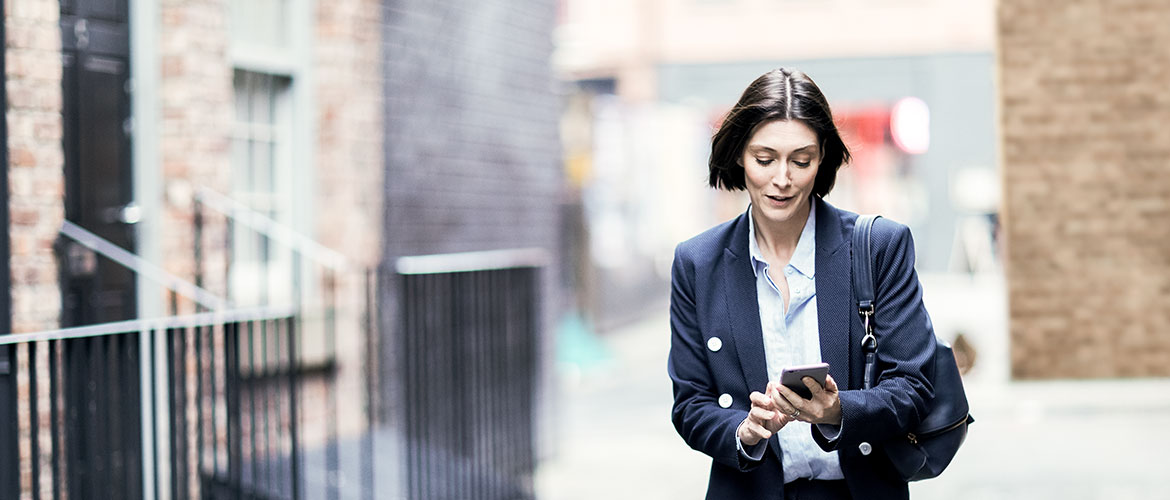 Frau geht Straße entlang und schaut auf ihr Smartphone