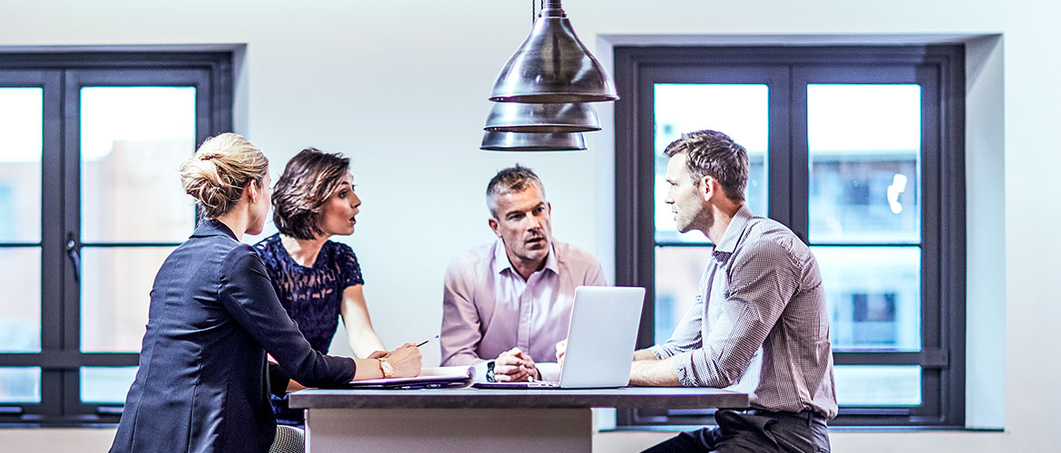 Vier Menschen sitzen an Bürotisch und diskutieren