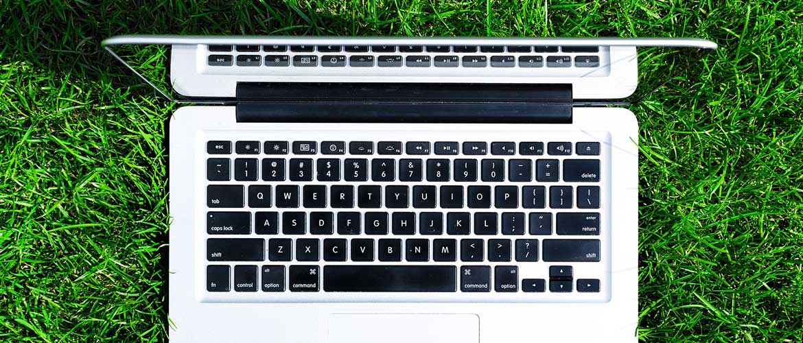 Aufgeklappter Laptop von oben, der auf einer grünen Wiese steht.